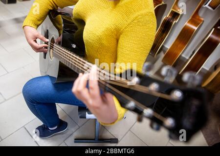 Woman trying, buying a new wood guitar in music instrument shop, instrumental concept Stock Photo