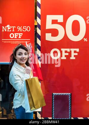 Beautiful woman in fashionable clothes shows listing sale on store showcases.Red sign on a shop window. Sale in a clothing store.Shopping, lifestyle c Stock Photo