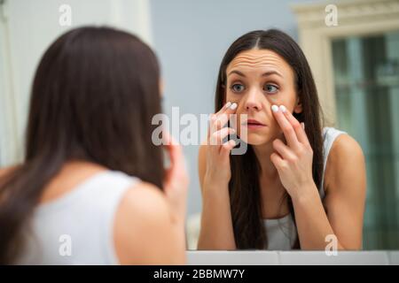 Tired woman looking at her eye bags in the bathroom. Stock Photo