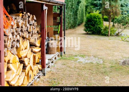 Wood stack with stacked firewood stock for fireplace heating in shed. Axe hanging on wooden beam of a hut on country farm or garden Stock Photo
