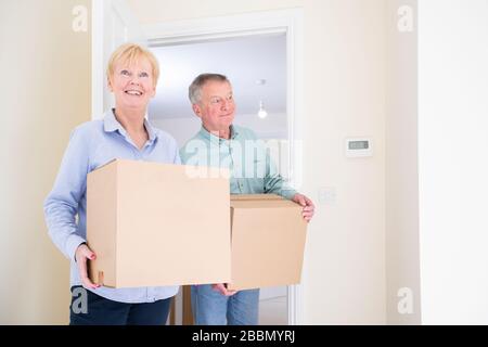 Senior Couple Downsizing In Retirement Carrying Boxes Into New Home On Moving Day Stock Photo