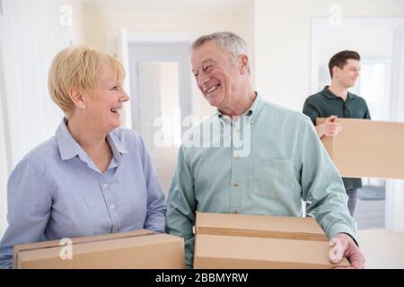 Senior Couple Downsizing In Retirement Carrying Boxes Into New Home On Moving Day With Removal Man Helping Stock Photo