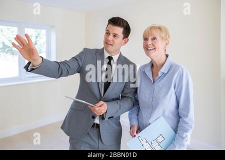 Realtor With Digital Tablet Showing Senior Woman Looking To Downsize Around Retirement Home Stock Photo