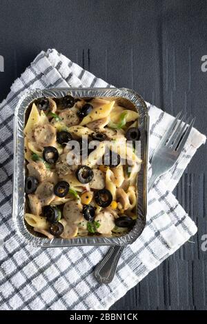 sausage penne pasta in a foil box on a chequered cloth Stock Photo