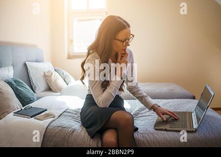 Businesswoman on business trip sitting in hotel room and working on laptop. Stock Photo