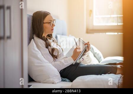 Businesswoman on business trip lying in hotel room and taking notes. Stock Photo