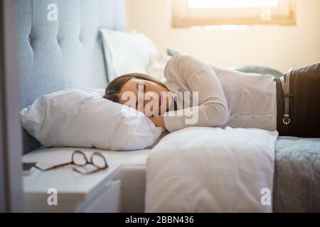 Tired businesswoman is sleeping dressed in hotel room. Stock Photo