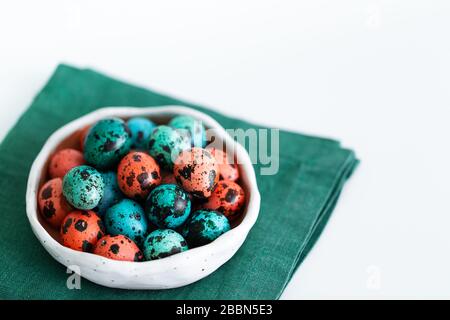 Painted red and blue quail eggs for Easter in small ceramic plate on green napkin on gray concrete background. Empty place for text and sign. Stock Photo