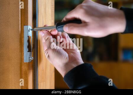 Carpenter repairing door lock. Installing a door handle. Handyman tightening door hinge . Hands of the repairman with a screwdriver. Locksmith screwin Stock Photo