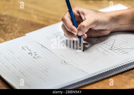 A teacher's hand holding a pencil and writing down a mathematical equation (formula) in a textbook Stock Photo