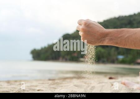 Play with sand on the beach. Sand is poured from the hands, against the backdrop of a tropical island Stock Photo