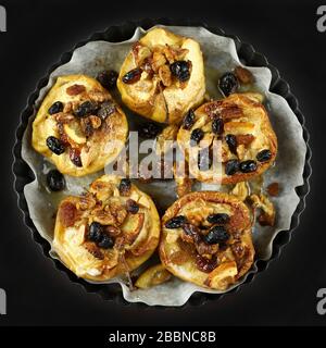 Concept of healthy dessert. Top view of baked apples stuffed with dried fruit, nuts, sultanas, cinnamon in a baking dish on dark background. Stock Photo