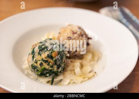 Two different kinds of bread dumplings with bacon and spinach plated on white pasta plate on wooden table, dinner for two persons Stock Photo