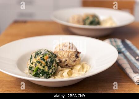 Two different kinds of bread dumplings with bacon and spinach plated on white pasta plate on wooden table, dinner for two persons Stock Photo
