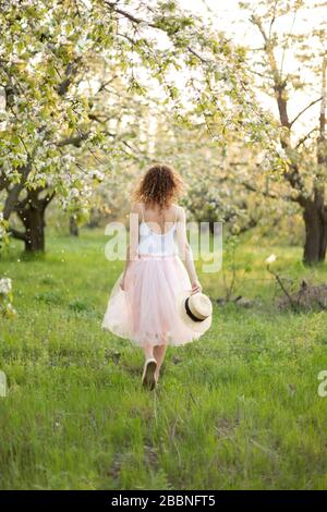 Young attractive woman with curly hair walking in a green flowered garden. Spring romantic mood. Stock Photo