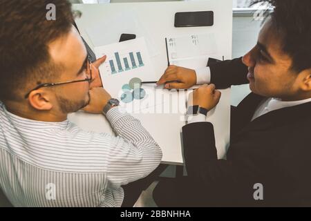 Young office worker sitting at desk, using computer. Two business man talking Stock Photo