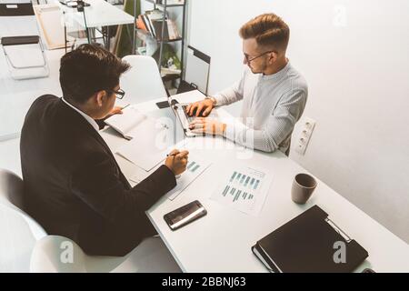 Young office worker sitting at desk, using computer. Two business man talking Stock Photo