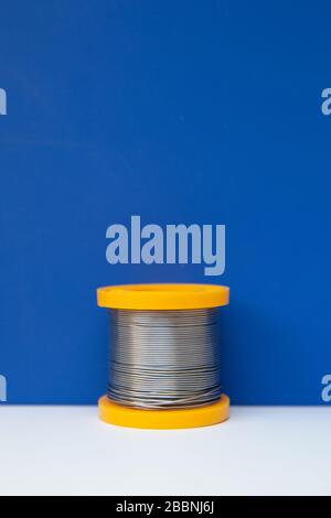 A yellow coil of solder stands in the frame. The coil stands on the white and blue media section.  Stock Photo