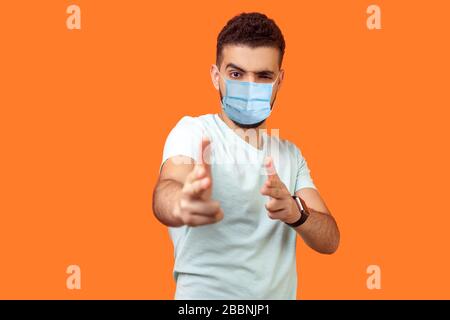 Gun gesture. Portrait of dangerous young brunette man with surgical medical mask in pointing with finger pistols at camera, pretending to shoot. indoo Stock Photo