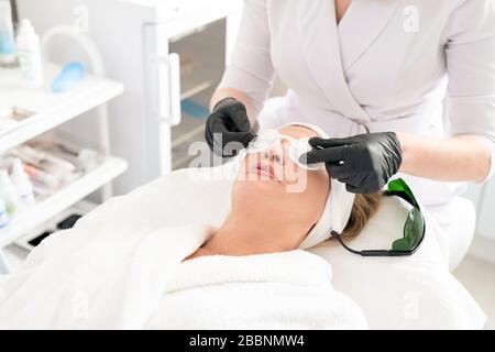 Close-up of unrecognizable beautician putting laser safety goggles on womens face while preparing client for laser surgery Stock Photo