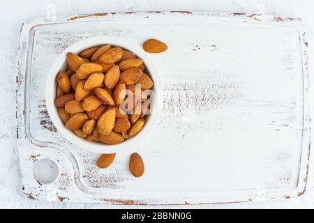 Top view almonds nuts in white bowl on a white wooden cutting board. Wooden background, Stock Photo