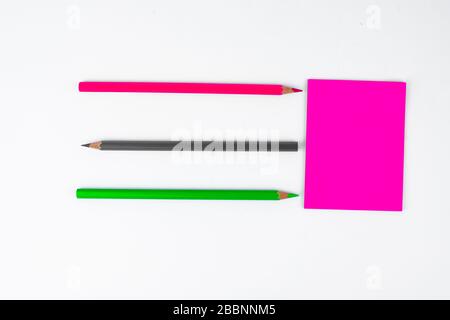 Three different colored wood pencil crayons pointing at a pink sticky paper note Stock Photo