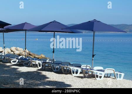 Blue umbrellas and chaise for relax and comfort on sea beach. Happy summer vacations and  tourism concept. Paid service on waterscape beaches. Stock Photo