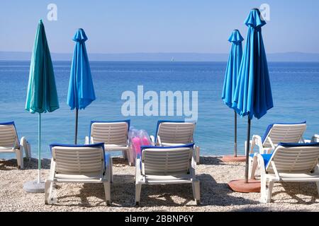 Blue umbrellas and chaise for relax on sea coast. Happy summer vacations and travel concept. Paid service on beaches. Stock Photo