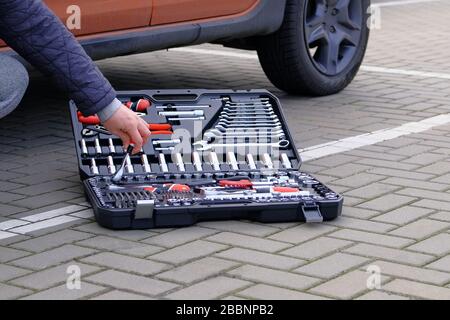 Tool set in box near the orange auto. Сar driver using different repair tools for repairing a vehicle. Automobile maintenance concept. Stock Photo