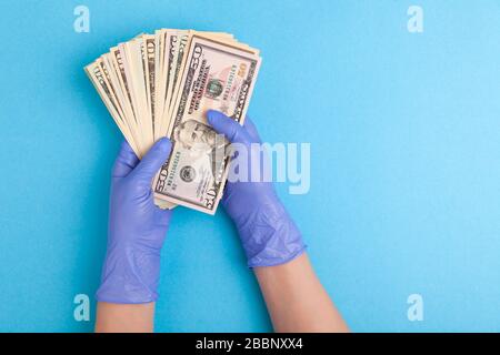 Hands in latex purple gloves hold  USA dollars banknotes on blue background, concept of world pandemic, horizontal, view from above, flat lay Stock Photo
