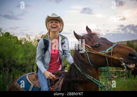 Happy young woman laughs with joy as she has fun horse riding in a rugged nature reserve. Stock Photo