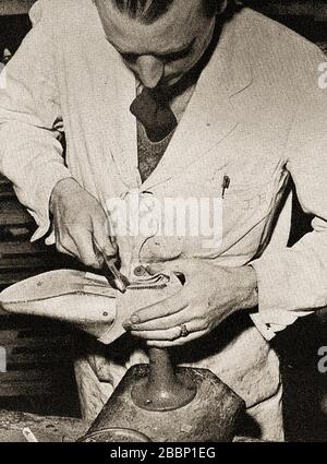 A 1930's image of a shoemaker using a last (stand shaped like a foot) to form the foot of a shoe. Stock Photo