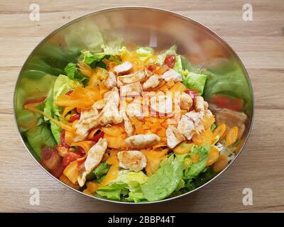 Bowl of mixed green lettuce salad & wooden background with sliced cut greens & vegetables carrots , tomato , roasted chicken pieces - light , healthy Stock Photo