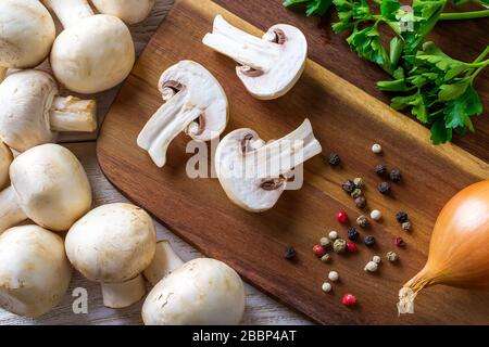 Three halves of champignons, pepper, onion and parsley on a wooden cutting board. Mushrooms as vegetable protein, raw food diet, vegetarianism. Stock Photo