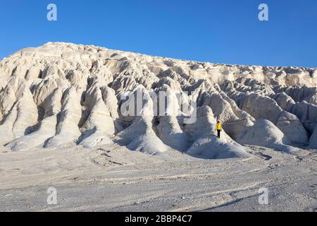 Woman in yellow jacket standing on white rock formations in the dramatic landscape at Tuzbair salt lake, Aktau, Mangystau, Kazakhstan, Stock Photo