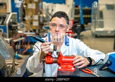 worker in metal processing plant grinds metal component on vise Stock Photo