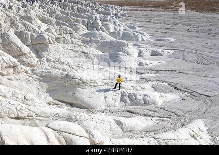 Woman in yellow jacket standing on white rock formations in the dramatic landscape at Tuzbair salt lake, Aktau, Mangystau, Kazakhstan, Stock Photo