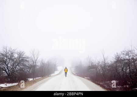 A lady walks alone on a gravel road during the emergency regulations regarding the coronavirus / COVID-19, on a foggy cold spring day. --- Stock Photo