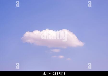 Blue sky in sunshine with a large white cloud and several small white clouds underneath like thought clouds or speech bubbles with plenty of copy spac Stock Photo