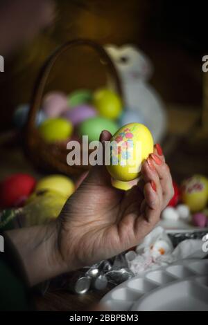 Woman hands is holding eggs with floral patterns. Preparing for Easter. Artist paints an Easter egg. Close-up. Selective focus. Copy space. Vertical o Stock Photo