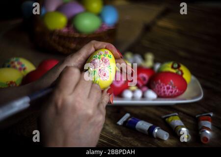 Woman hands painting eggs with floral patterns. Preparing for Easter. Artist paints an Easter egg. Close-up. Selective focus. Copy space. Horizontal o Stock Photo