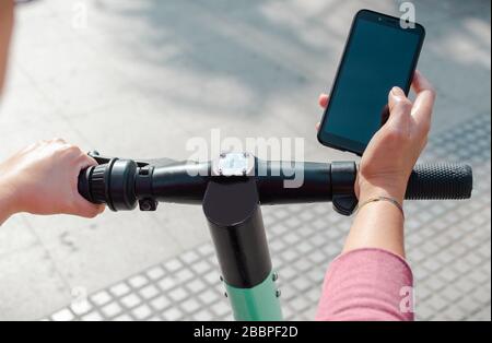 Unrecognizable person using smartphone to pay for rental electric scooter while standing on modern city street Stock Photo