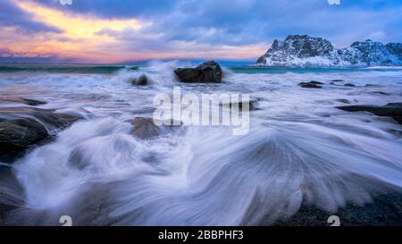 Ocean waves washing over coastal rocks with sunset sky in the background Stock Photo