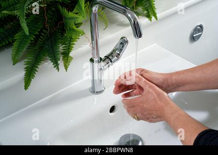 A woman washing her hands at a domestic sink. Tap with water flowing onto hands and basin behind. Bathroom or restroom setting. Stock Photo