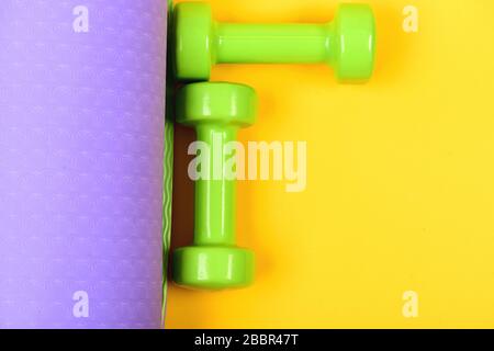 Barbells in small size on yoga mat, close up. Healthy shape and sport concept. Dumbbells made of light green plastic on yellow and purple background, top view. Shaping and fitness equipment Stock Photo