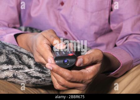 Hand holding remote control sitting on sofa . Stock Photo