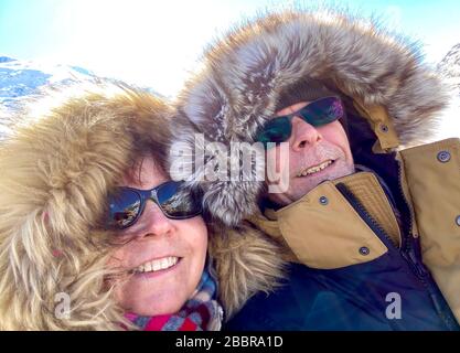 Closeup of a couple dressed up in parkas with furry hoods out for a walk in the winter sun Stock Photo