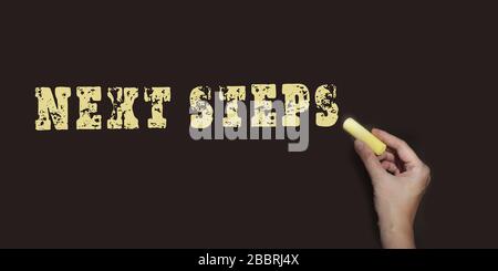 Next steps written with yellow chalk on blackboard. Business startup proccess concept Stock Photo