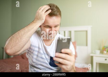 Young man feelling worried while holding phone or smartphone in his hand. One hand in his head. Big troble concept face. Stock Photo
