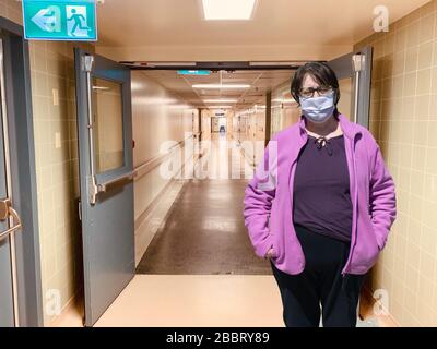 Elderly woman in protective medical mask isolated against empty hospital corridor. Coronavirus elderly advice. Safety old men. Transmission of virus t